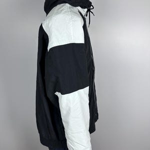 May include: A black and white color block jacket with a zipper closure and a hood. The jacket has a white panel on the right shoulder and a white panel on the right sleeve.
