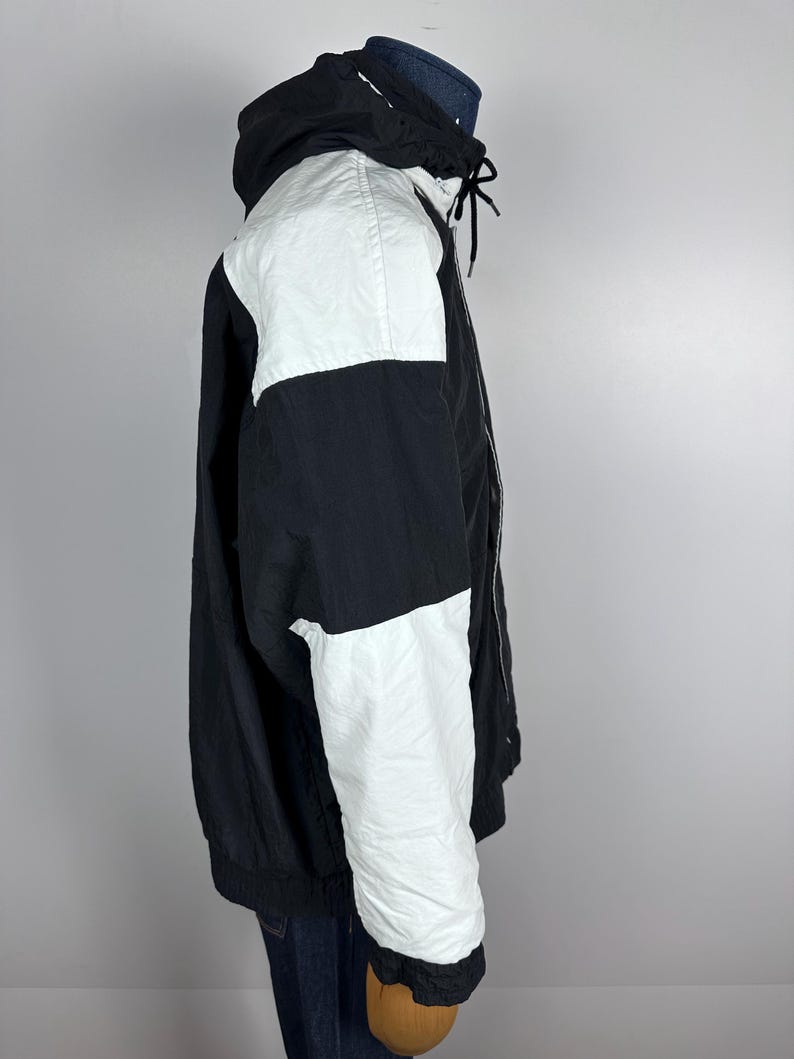 May include: A black and white color block jacket with a zipper closure and a hood. The jacket has a white panel on the right shoulder and a white panel on the right sleeve.