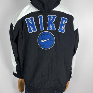 May include: Black and white Nike windbreaker jacket with a blue basketball and the word "NIKE" in white lettering on the back.