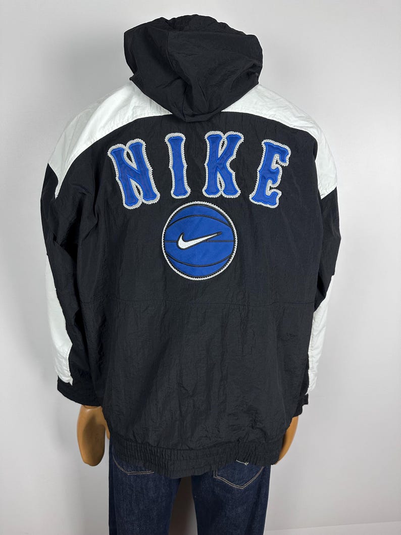 May include: Black and white Nike windbreaker jacket with a blue basketball and the word "NIKE" in white lettering on the back.