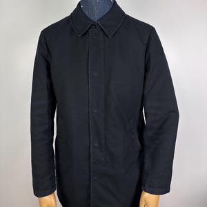 May include: A black long-sleeved jacket with a button-up front and a collar. The jacket has two pockets on the front and a single pocket on the left sleeve.