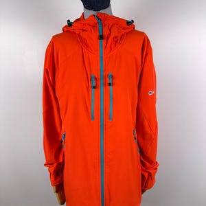 May include: A bright orange hooded jacket featuring a contrasting light blue full-length front zipper and two vertical chest pockets with matching light blue zippers. The jacket includes a hood with adjustable drawstrings and a small logo on the sleeve.