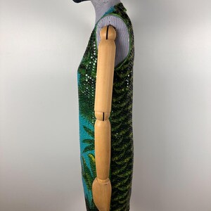 May include: A sleeveless dress with a tropical design. The dress features a vibrant pattern of green palm leaves and blue accents, embellished with sequins. The dress is displayed on a mannequin.