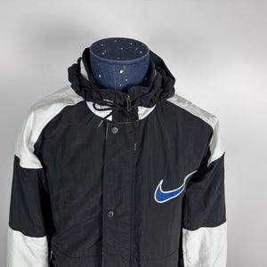 May include: A black and white windbreaker jacket with a blue Nike swoosh logo. The jacket has a zipper closure and a hood.