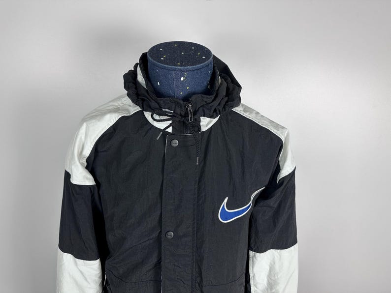 May include: A black and white windbreaker jacket with a blue Nike swoosh logo. The jacket has a zipper closure and a hood.