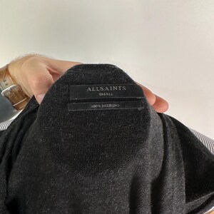 May include: Dark gray merino wool sweater with a label that reads "ALLSAINTS SMALL 100% MERINO". The sweater is a small size and appears to be a lightweight knit. The fabric is a solid dark gray color.