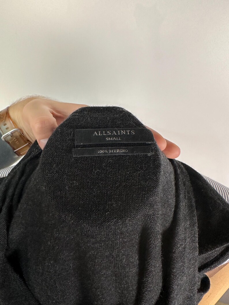 May include: Dark gray merino wool sweater with a label that reads "ALLSAINTS SMALL 100% MERINO". The sweater is a small size and appears to be a lightweight knit. The fabric is a solid dark gray color.