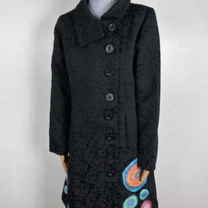 May include: Black long-sleeved coat with a collar and a row of buttons down the front. The coat has a floral pattern and a colourful abstract design on the bottom.