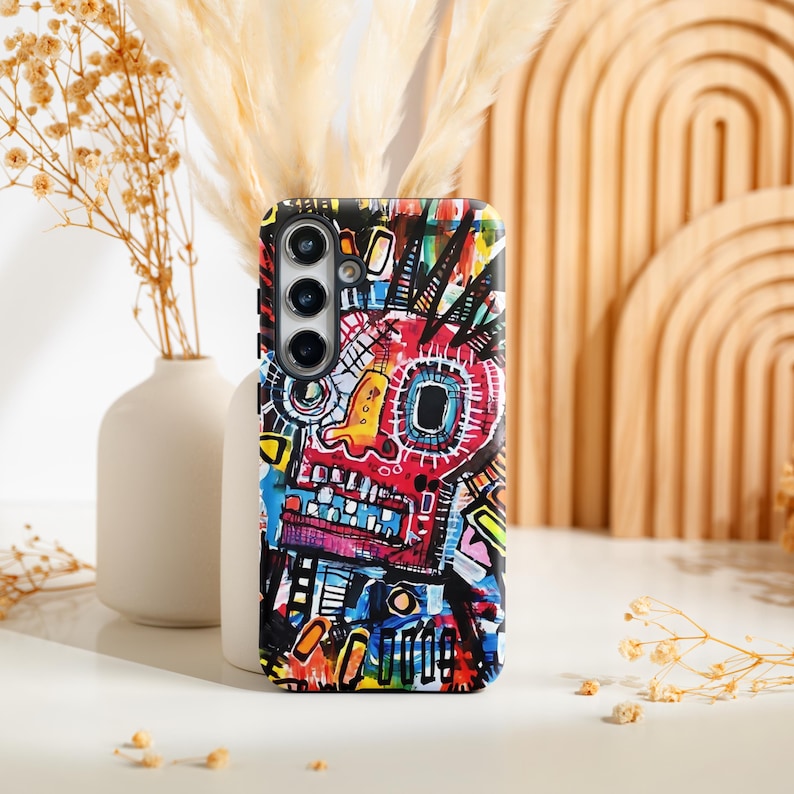 Pu&ograve; includere: Una custodia per telefono colorata con un design a volto astratto. La custodia presenta un vivace mix di rosso, giallo, blu e nero, creando un look audace e artistico. Il design ricorda l'arte dei graffiti.