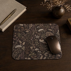 May include: A rectangular mouse pad featuring a dark brown background with a detailed botanical print of various wildflowers, grasses, and leaves in muted tones of cream, beige, and sage green, with a dark brown wireless computer mouse on top.