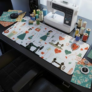 May include: A white sewing machine sits on a black desk, surrounded by spools of thread in various colors. A long, patterned desk mat features illustrations of sewing machines, hearts, and women in dresses. Fabric scraps and sewing tools are also visible.