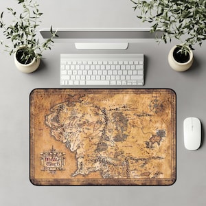 May include: A rectangular mousepad featuring a detailed map of Middle-earth, with the text "Middle Earth" in a decorative frame. The map is in shades of brown and tan, with black lines indicating geographical features. A white mouse and keyboard are visible.