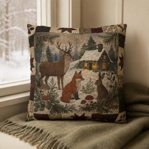 May include: A square throw cushion featuring a woven tapestry design of a winter forest scene with a deer, a fox, and a rabbit. The central image shows a snow-covered cabin with lit windows, surrounded by pine trees, mushrooms, and a patchwork border.