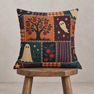 Könnte beinhalten: Ein quadratisches Zierkissen mit einem Patchwork-Design aus abwechselnden Feldern. Das Muster zeigt Illustrationen eines Apfelbaums, Geistern, Sternen und Herbstblättern in Orange-, Dunkelrot-, Schwarz- und Cremetönen auf strukturiertem Stoff.