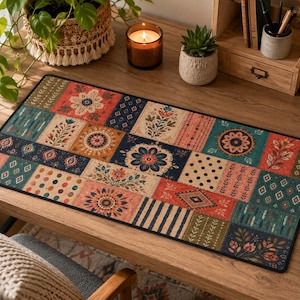 Peut inclure: Un tapis de bureau rectangulaire présentant un motif patchwork composé de divers designs floraux, géométriques et rayés dans des tons de rouge, bleu marine, sarcelle et crème. Le tapis a une bordure noire et est posé sur une surface en bois.