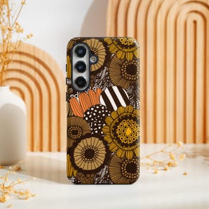 Puede incluir: Una funda de teléfono con un estampado floral en tonos marrones, amarillos, naranjas y blancos. El diseño presenta flores estilizadas y formas circulares. La funda tiene un módulo de cámara con tres lentes.