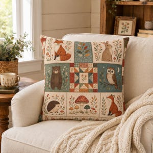 Könnte beinhalten: Ein quadratisches Zierkissen mit Patchwork-Design, das einen Fuchs, einen Hasen, einen Bären, eine Eule, einen Igel und Pilze zeigt. Das Muster enthält florale Elemente und einen zentralen geometrischen Sternblock in Braun-, Rot- und Blautönen.