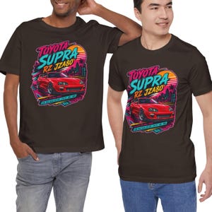 May include: Two brown t-shirts featuring a graphic of a red Toyota Supra RZ JZA80 car. The design includes the text "Toyota Supra RZ JZA80" in a retro style with a sunset and palm trees.
