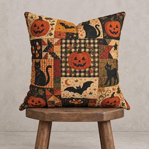 May include: A square throw pillow featuring a patchwork design with Halloween motifs including orange jack-o'-lanterns, black cats, bats, stars, and candy corn on a background of black and white buffalo check and various autumn-toned fabric patterns.