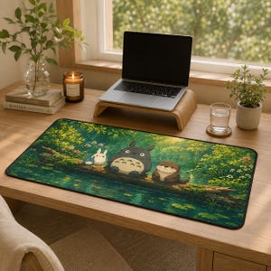May include: A rectangular desk mat featuring a vibrant, detailed illustration of a forest scene with a large gray creature, a small white creature, and a brown otter sitting on a log over a pond surrounded by lush green foliage and flowers.