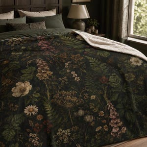 May include: A dark green blanket featuring a detailed botanical print of various wildflowers, ferns, and foliage in muted earth tones. The blanket has a soft, cream-coloured sherpa fleece lining visible at the folded top edge, providing texture.