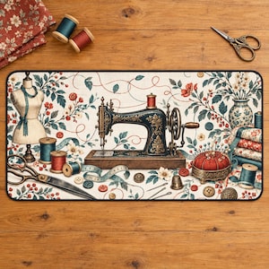 Può includere: Un tappetino da scrivania rettangolare con una macchina da cucire vintage, un manichino, rocchetti di filo, forbici, bottoni e un puntaspilli. Il design è su uno sfondo color crema con un motivo floreale di fiori rossi e foglie verdi.