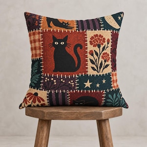 Peut inclure: Un coussin carré au motif patchwork composé d'illustrations tissées de chats noirs, de fleurs orange, d'un croissant de lune, d'étoiles et de motifs à carreaux dans des tons rouge, noir, violet et crème avec des bordures style point de couture.
