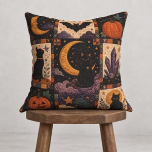 May include: A square throw pillow featuring a patchwork design with black cats, crescent moons, pumpkins, bats, and purple crystals. The quilted fabric displays a dark color palette with orange, yellow, and purple accents in a repeating celestial pattern.
