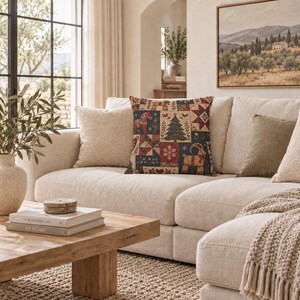 May include: A square throw pillow featuring a patchwork design with holiday motifs including a Dala horse, a Christmas tree, a goat, and geometric star patterns in shades of red, navy blue, green, and cream on a textured fabric surface.