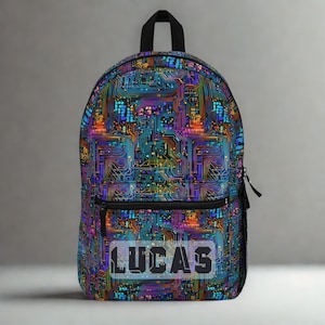 Könnte beinhalten: Ein Rucksack mit einem lebendigen Leiterplattenmuster in Blau-, Lila-, Orange- und Grüntönen. Das Wort "LUCAS" ist in weißen Blockbuchstaben auf der Vordertasche abgebildet. Er hat einen schwarzen Tragegriff, Reißverschluss und eine Seitentasche.