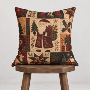 Può includere: Un cuscino quadrato con design patchwork caratterizzato da un'illustrazione centrale di Babbo Natale che tiene in mano un albero di Natale e un sacco di regali. Il motivo include agrifoglio, stelle, renne e pacchetti in rosso, verde e crema.