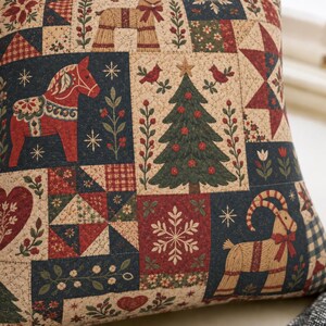 May include: A square throw pillow featuring a patchwork-style print with holiday motifs including a red Dala horse, a green Christmas tree, a tan goat, red hearts, snowflakes, stars, and floral patterns in a color palette of red, navy blue, and tan.