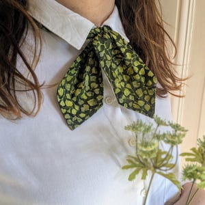 May include: A white collared shirt with a green and yellow patterned bow tie. The bow tie has a leaf design.