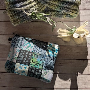 Könnte beinhalten: Ein blaues und grünes Strick Stirnband mit einem gedrehten Design, eine kleine blaue und weiße Patchwork Stofftasche mit Reißverschluss und eine weiße Blume auf einem Holz Hintergrund.