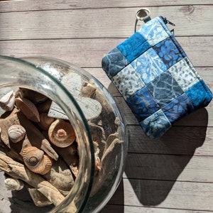 Könnte beinhalten: Ein Glasgefäß gefüllt mit Treibholz und Muscheln, mit einer blauen und weißen Patchwork-Stofftasche mit Reißverschluss an der Seite, auf einer Holzoberfläche.