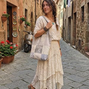 Könnte beinhalten: Eine beigefarbene Leinenbluse mit Dreiviertelärmeln, ein cremefarbener, gestufter Spitzenrock mit asymmetrischem Saum und eine Patchwork-Tragetasche aus verschiedenen grauen, weißen und beigefarbenen Stoffquadraten mit unterschiedlichen Mustern.