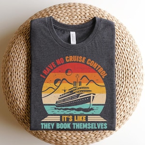 May include: Dark gray t-shirt with a circular graphic featuring a cruise ship on water, mountains, and a sunset. The text reads "I HAVE NO CRUISE CONTROL IT'S LIKE THEY BOOK THEMSELVES."