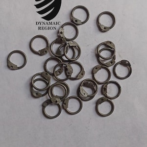 Może przedstawiać: Stosik srebrnych metalowych pierścieni, każdy z małym otworem. Pierścienie są ułożone w przypadkowy wzór na białym tle.