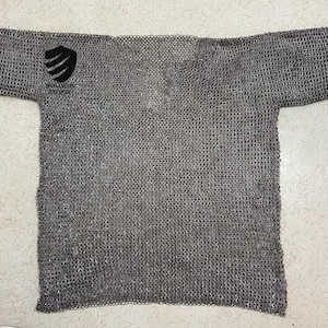 May include: A gray chainmail shirt with a v-neck and short sleeves. The shirt has a small black patch on the left shoulder.