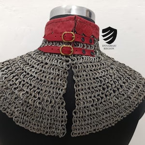 May include: A silver chainmail collar with a red leather trim and gold buckles. The collar is on a black mannequin.