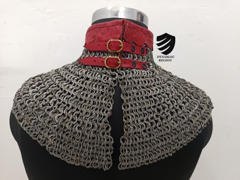May include: A silver chainmail collar with a red leather trim and gold buckles. The collar is on a black mannequin.