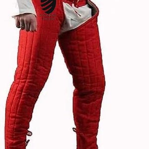 Può includere: Armatura per gambe medievale trapuntata rossa. L'armatura è di un colore rosso vibrante e presenta un motivo trapuntato. L'armatura per le gambe è progettata per essere indossata con una camicia bianca e scarpe marroni. L'armatura è legata in vita con una chiusura con lacci.