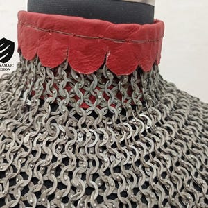 May include: A close-up of a silver chainmail collar with a red leather trim. The leather trim has a scalloped edge.