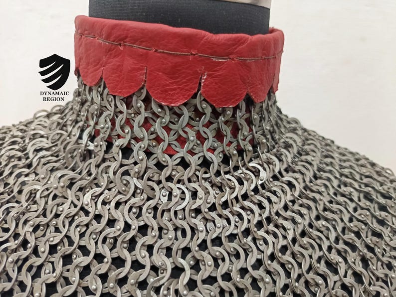 May include: A close-up of a silver chainmail collar with a red leather trim. The leather trim has a scalloped edge.