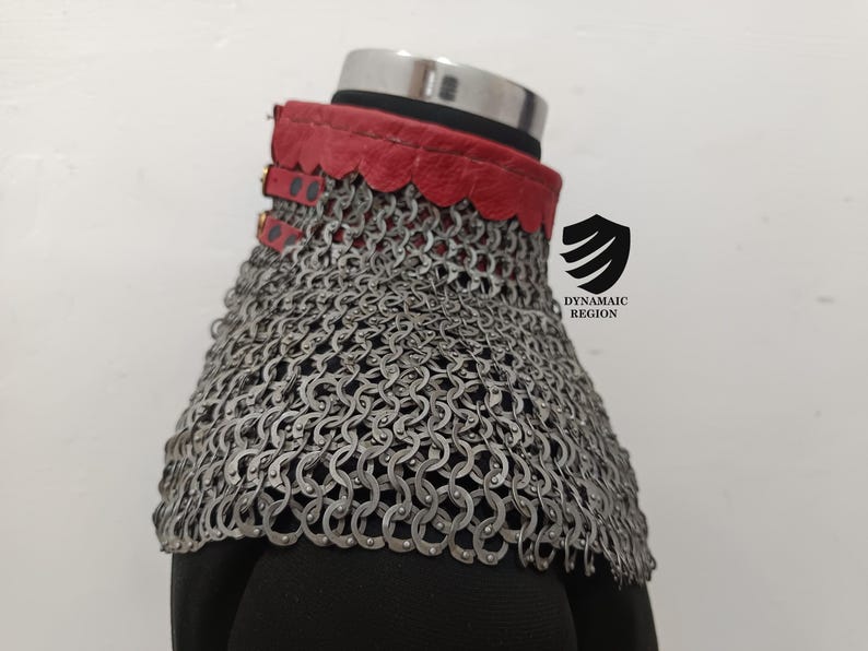 May include: A red leather collar with a chainmail neck guard. The collar has a scalloped edge and is fastened with buckles. The chainmail is made of small, interlocking metal rings.