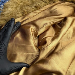 May include: The inside of a brown faux fur jacket with a gold satin lining. The lining has a small pocket.