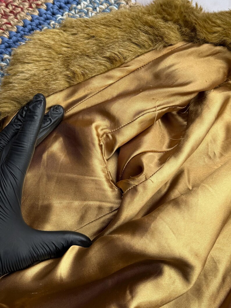 May include: The inside of a brown faux fur jacket with a gold satin lining. The lining has a small pocket.