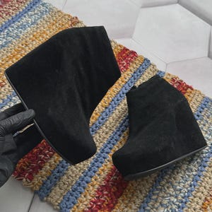 May include: A pair of black suede ankle boots featuring a high wedge heel and a thick platform sole. The boots have a smooth, solid black exterior with a rounded toe design and a high-cut ankle silhouette, showcasing a clean and simple aesthetic.