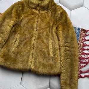 May include: A soft, plush faux fur jacket in a muted olive green color. The jacket has a high collar and a zipper closure.