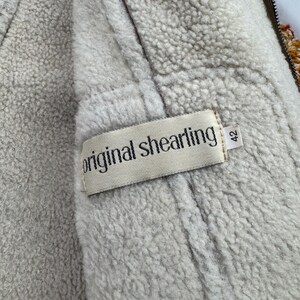 May include: Close-up of a vintage shearling jacket interior. The jacket features a cream-colored, fluffy lining and a brown exterior. A tag reads "original shearling" with the size "42".
